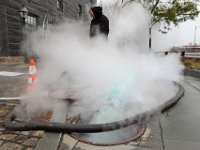 Steam billows upward from the manhole in the foreground, as John Davis of Green Mountain Pipeline is monitors the meters while hot steam shrinks the liners to the freshly cleaned sewer line in front of the Buzzards Bay Coalition building in downtown New Bedford.  PHOTO PETER PEREIRA