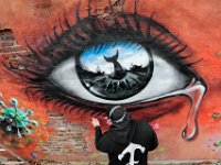 Graffiti artist Jeff Saint works on a mural featuring a crying eye with the icons of the whaling city reflected in its pupil, surrounded by coronavirus spores.  He and fellow graffiti artist, Ryan McFee, are painting the piece on a building adjacent to the Custom House Square in New Bedford with the hope of eventually replacing the spores with flowers are the virus is defeated.  PHOTO PETER PEREIRA