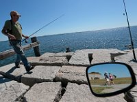 Stanley Bisaillon walks over to put some fresh bait on the hook while from a pier at Fort Taber Park in the south end of New Bedford, while in the mirror of his motorized bicycle, a couple can be seen wallking the paths behind Fort Rodman.  PHOTO PETER PEREIRA