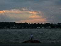 A man standing on a pier overlooking Clark's Cove in the south end of New Bedford takes in the sight, ss the setting sun send rays of light through the clouds in the distance.  PHOTO PETER PEREIRA