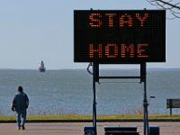 A sign urges residents to stay home as a man makes his way across the Fort Phoenix parking lot in Fairhaven.  PHOTO PETER PEREIRA