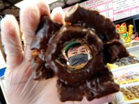 Alexander Hong, owner of the recently opened Daily Made Donuts on Rockdale Avenue in New Bedford, holds up a custom old fashion donut with chocolate frosting. PHOTO PETER PEREIRA