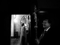 Eucharistic minister, Donal Buckley, holds a crucifix as Father Michael Racine, is seen looking to see if everything is in place before conducting a funeral mass at St Lawrence Martyr Church on County Street in New Bedford which is celebrating its 200th anniversary,