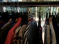 A woman is seen walking up Purchase Street in New Bedford, as seen through a gap in the hangers of women's clothing for sale inside The MadLila clothing store in downtown New Bedford.
