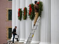 Tony Frothing places holiday wreaths on the collunade of the Best Banc & Co building on William Street in downtown New Bedford as a worker makes his way into the historic building.
