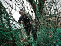 Jose Bras cuts away the section of the net that has rotted away, as he makes repairs to the nets aboard the fishing boat Hera, docked in New Bedford.