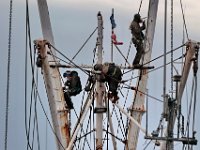 Three workmen find themselves high above Fleet Marina in New Bedford as they remove the rust from the outriggers of a fishing boat, before applying a fresh coat of paint.