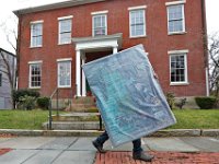 A man makes his way up William Street in downtown New Bedford holding a wrapped art piece.