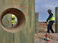 Helder Baptista, left (seen through one of the holes that he and fellow members of New Bedford DPI made) keeps his eye on the horizontal alignment for the hole that Danny Pacheco is making using a drill with an auger on one of the posts that will become part of a future fishermen memorial.  The memorial will feature an anchor with a heavy chain running through the holes they are making.  PETER PEREIRA/The Standard-Times