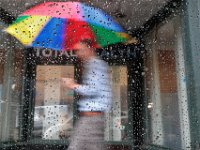 A man with a colorful umbrella walks past a roan soaked car window, as he makes his way down William Street in New Bedford on a rainy day.