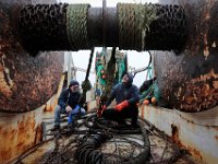 Edward Combs, left, joins Captain Antonio Cravo in preparing the gear for a new net they will install on the huge drum in front of them aboard the fishing boat United States docked in New Bedford.