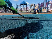 Javier Munoz is joined by the shadow of Antonio Barradas as they insall the colorful, rubbery, soft surface at the new playground they are constructing on Apponagansett Beach in Padanaram.