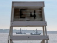 A fishing boat heads out to sea, as another comes into New Bedford harbor, as seen through the gap of a lifeguard chair at East Beach in New Bedford.