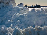 The Palmers Island lighthouse is seen in the distance, through the section atop the large mountain of snow plowed at State Pier in New Bedford.  PETER PEREIRA/The Standard-Times