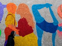 A woman walks past a colorful mural painted on the wall of the Police Station on Sears Court in downtown New Bedford.
