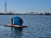Two dock workers have gone back in time, using a blue tarp as a sail, to navigate from one dock to another farther down North harbor in New Bedford.
