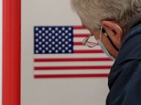 The American flag on the wall of the voting station is seen in the glasses of a man casting his vote at the Normandin Middle School voting station in New Bedford. [ PETER PEREIRA/THE STANDARD-TIMES/SCMG ]