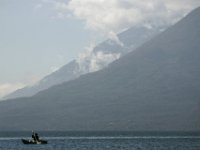 A crab fisherman paddles his wooden boat around Lake Atitlan in the background Toliman volcano and Atitlan volcano loom.  Scene around Lake Atitlan in Guatemala.