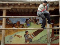A man prepares his booth for market day while in the background a mural on town hall depicts life in Chichiquastenango, Guatemala. Preparation for the next days market.