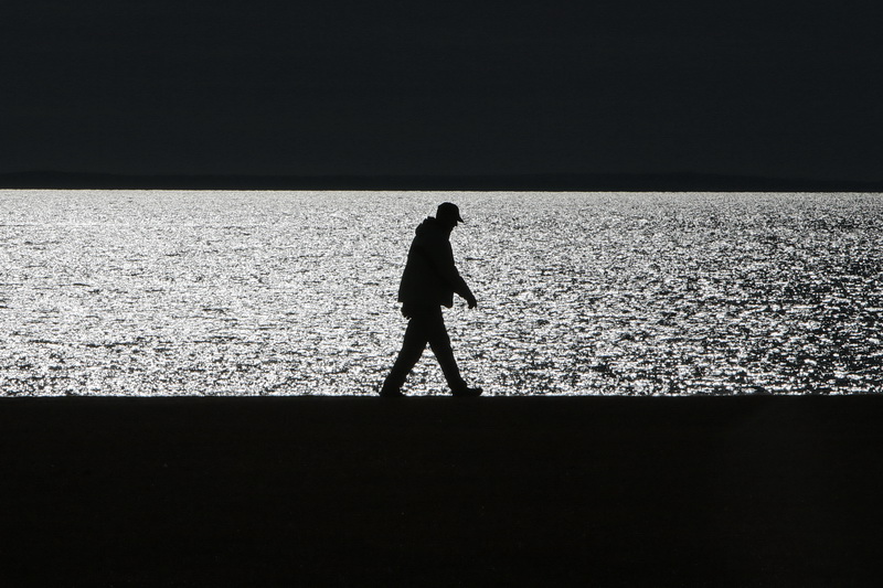 The early morning sun shimmers across the waters of Buzzards Bay beyond, as a man makes his way across Fort Taber Park in the south end of New Bedford, MA between the horizon beyond, and the ground below. 