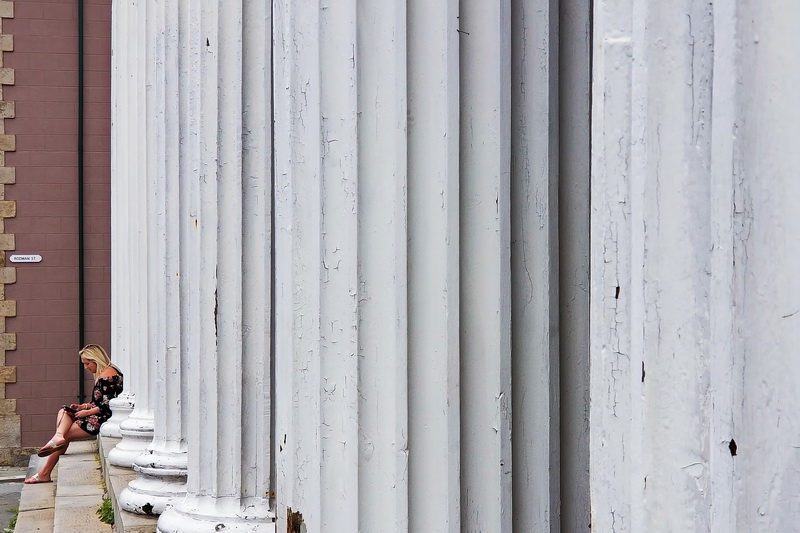 A woman sits on the steps of the J.J. Best Banc & Co. building on N Water Street in downtown New Bedford, MA in front of the colonnade of white fluted columns.   PHOTO PETER PEREIRA