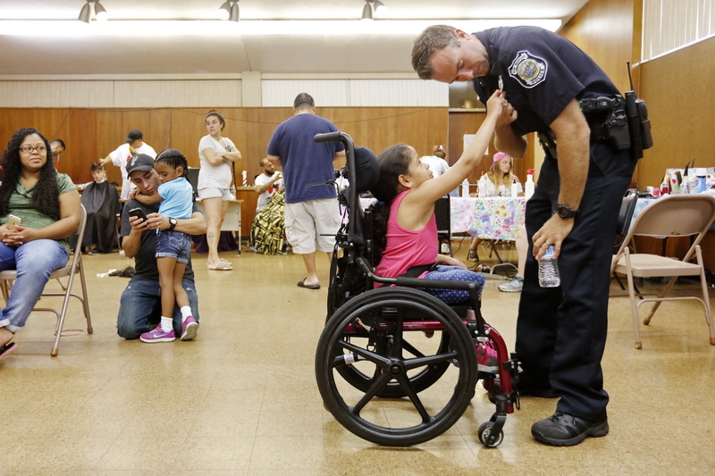 New Bedford police officer, Tom Chevalier, bends down so that Amalya Romero, 8, can touch his badge at the first annual New Bedford Cuts for Kids held at the Wilks Library on Acushnet Avenue, New Bedford, MA. PHOTO PETER PEREIRA