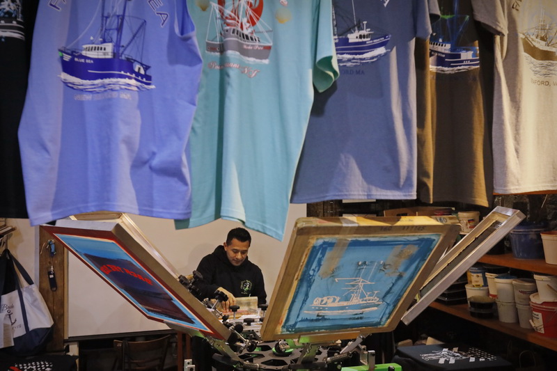 Carlos Chamorro is seen between the screen printing machine, printing new t-shirts in preparation for the Holiday season at The Landing in downtown New Bedford, MA. PHOTO PETER PEREIRA