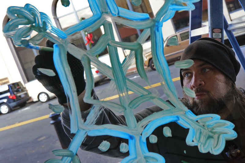 Local artist, Noah Barrett, paints a snowflake on the windows of the Harbor Hotel on Union Street in downtown New Bedford in preparation for the holiday season. PHOTO PETER PEREIRA