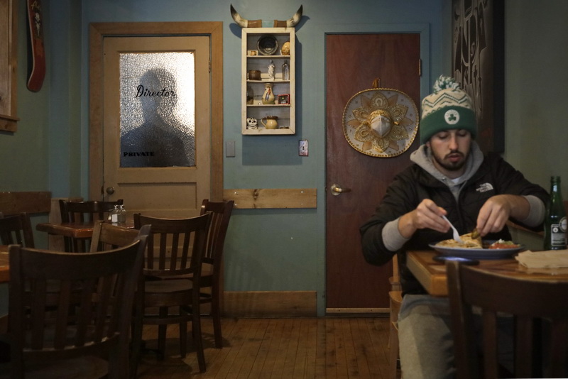 A patron of No Problemo in downtown New Bedford, MA enjoys lunch, as a shadow figure can be seen passing behind a door's glass pane in the back of the dining area.   PHOTO PETER PEREIRA