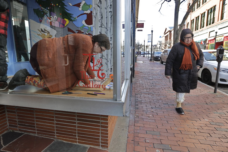 A pedestrian walks past as Jenny Newman-Arruda co-owner of The Gallery on William Street in downtown New Bedford, changes the Christmas themed painting on the store front of her gallery, with a wooded pattern wallpaper in preparation for the opening of the Birds of New England Art show on February 14th.  PHOTO PETER PEREIRA