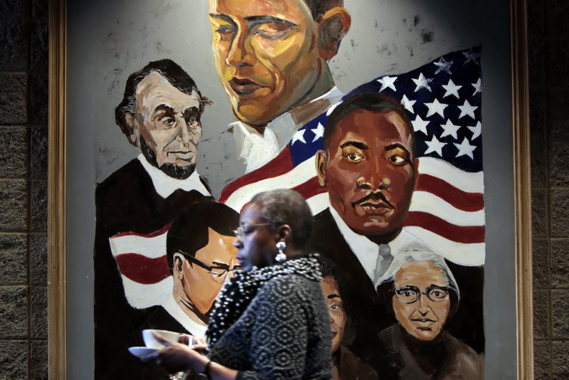 A worman walks past a painting of civil rights leaders hanging outside the hall where the annual Dr. Martin Luther King Jr. Breakfast was held at UMass Dartmouth.    PHOTO PETER PEREIRA