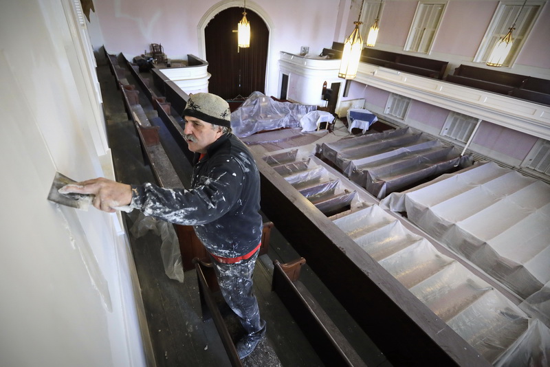 High above the altar and plastic covered pews below, Charles Hauck applies some joint compound to the walls of the mezzanine as he and fellow restorers work on repairing the interior walls of the First Baptist Church on William Street in New Bedford, MA.  The church which was built in 1829 is on the U.S. National Register of Historic Places and is featured prominently on the city seal. PHOTO PETER PEREIRA