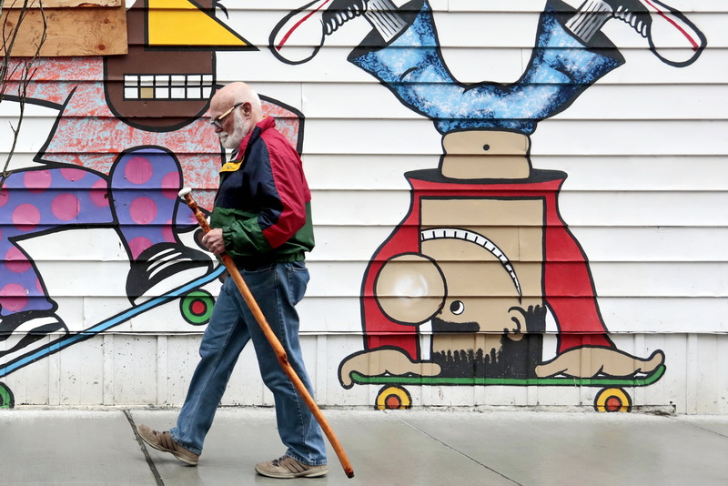 A man with a walking stick makes his way past a mural painted on the side of a building on Pleasant Street in downtown New Bedford.    PHOTO PETER PEREIRA