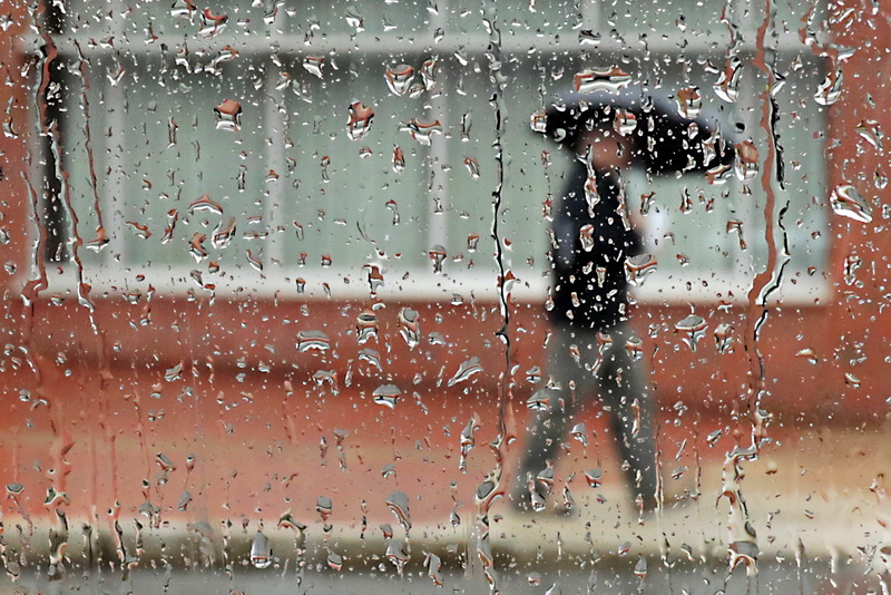 A pedestrian walks with umbrella in hand past a rain soaked window of a vehicle on Pleasant Street in New Bedford, MA.   PHOTO PETER PEREIRA