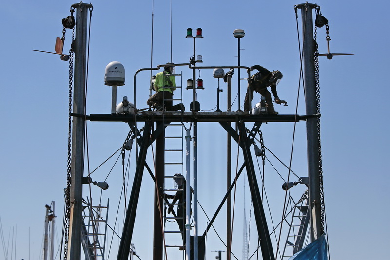 Three painters find themselves high above the deck of a fishing boat docked in New Bedford, MA harbor, as they scrape the existing paint in preparation for a fresh coat.  PHOTO PETER PEREIRA