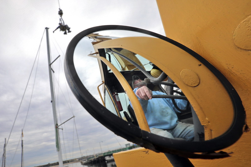 Jim Tripp, owner of Davis & Tripp Marina, is reflected on the mirror of the crane that he is operating to lift Dustin Lavalley up to the top of the mast in order to install the wind vane, on the sailboat they are rigging at the Dartmouth, MA marina.  PHOTO PETER PEREIRA