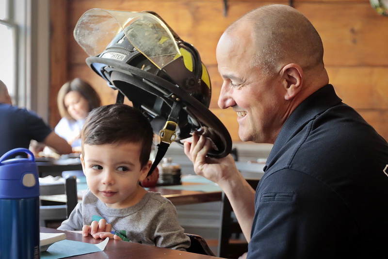 New Bedford firefighter Ronald Crowell who was grabbing a cup of coffee at Tia Maria's European Cafe, offers to show his firefighter helmet to Karter Conchinha, 2, who was there having breakfast with his family.  PHOTO PETER PEREIRA