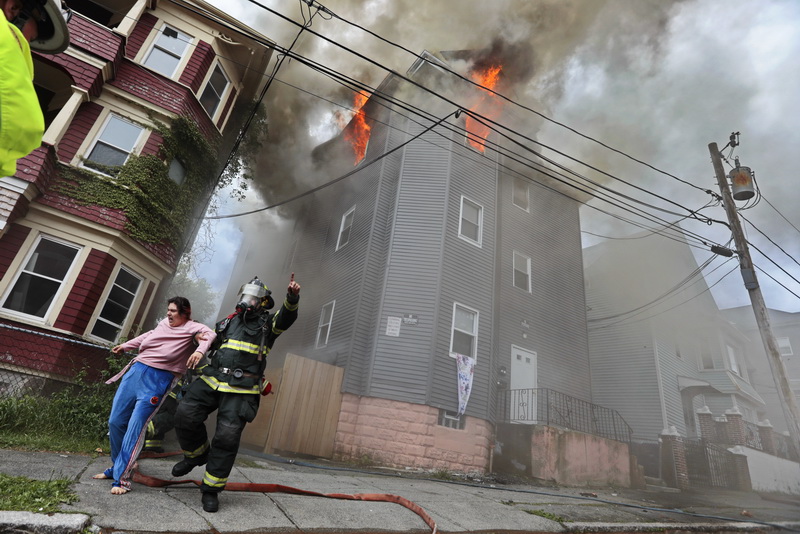 A New Bedford firefighter rescues a woman who was sleeping on the second floor of a three residence building which caught fire on Clark Street in New Bedford, MA. The woman was taken in an ambulance for smoke inhalation.  PHOTO PETER PEREIRA