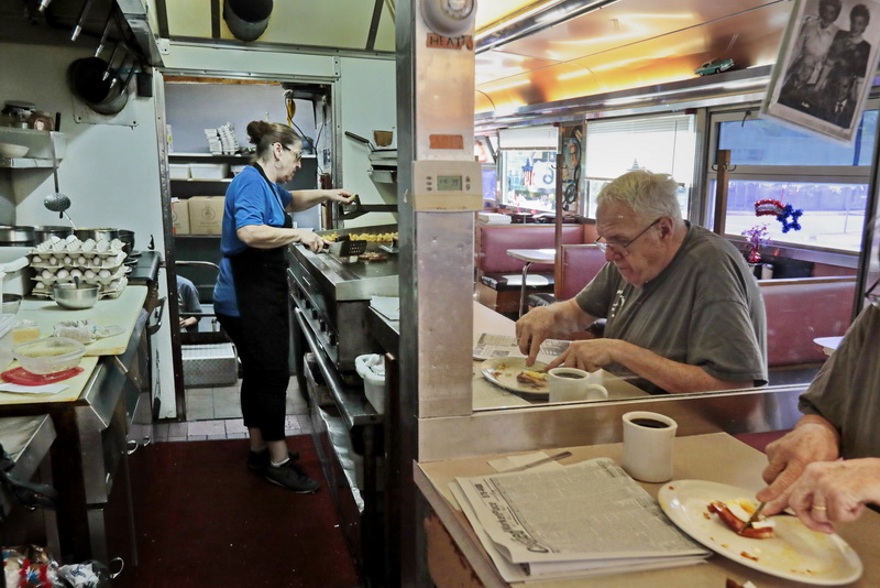 Sherry Massa is seen in the kitchen preparing breakfast for a patron, as Tim Mitchell is reflected in the mirror, enjoying his breakfast at the counter of the Angelo's Orchid diner on Rockdale Avenue in New Bedford, MA.  PHOTO PETER PEREIRA