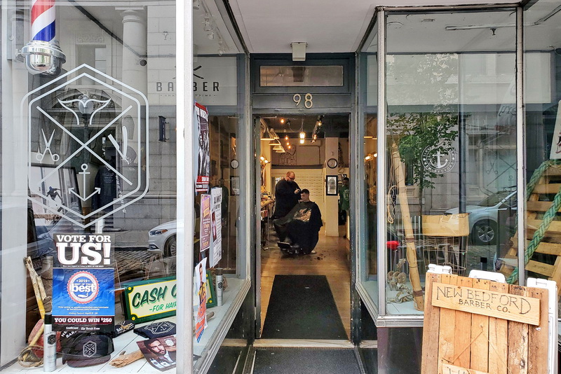 Jacob Henriques gives Michael Stemper a haircut, as seen through the open door of the New Bedford Barber Co. on William Street in downtown New Bedford, MA.   PHOTO PETER PEREIRA