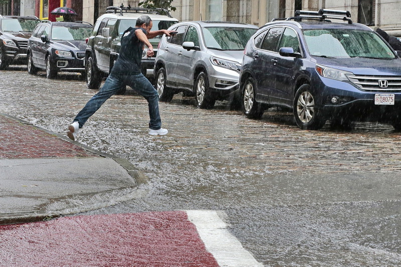 A man leaps over the water cascading down William Street in downtown New Bedford, MA as heavy rains fall across the region.   PHOTO PETER PEREIRA