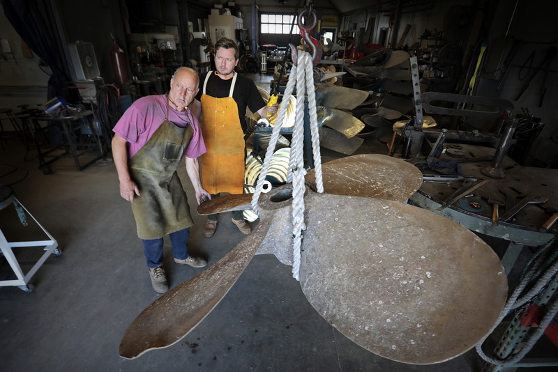 Mihkel Valm, left, co-owner of Marine Propeller Service in Fairhaven, and Andrius Limantas, take delivery of the propeller of the fishing boat Azores which needs to be repaired as can be seen from the kink at the edge of the blade on the bottom left.  PHOTO PETER PEREIRA