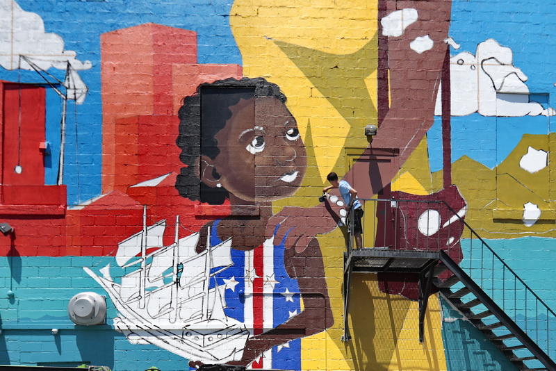 David Guadalupe paints the beads on the woman's bracelet as he works on a mural with a Cape Verdean theme,  painted on the side of the Bisca Club on Acushnet Avenue in New Bedford, MA. PHOTO PETER PEREIRA