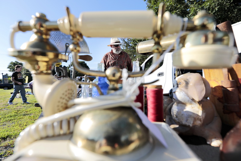 A customer walks in the background, as Steve Long puts out the over one thousand items, including the old style telephone, on his tables at the weekly Mattapoisett Flea Market held every Tuesday in front of the Knights of Columbus Hall on Route 6 in Mattapoisett, MA.    PHOTO PETER PEREIRA