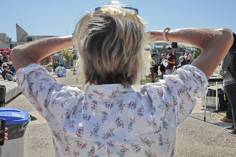 An attendee sheilds her eyes from the sun as she listens to Erik Andrade, left speak, as Aidan Fitzsimons, left, can be seen on the other side holding an inflatable earth, during a Climate Strike held at UMass Dartmouth.  PHOTO PETER PEREIRA