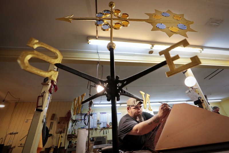 TJ Marshall works on the copper top of a cupola he is making at Cape Cod Cupola on Route 6 in Dartmouth, MA.  In the foreground a completed sun themed weathervane that TJ just finished installing gold leaf to. PHOTO PETER PEREIRA