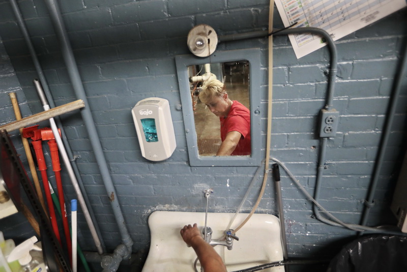 Susan Martins is reflected on the mirror in front of the sink she is pulling hot water from, in preparation to clean up a milk spill a student made in a classroom at the Devalles Elementary School in New Bedford, MA. PHOTO PETER PEREIRA