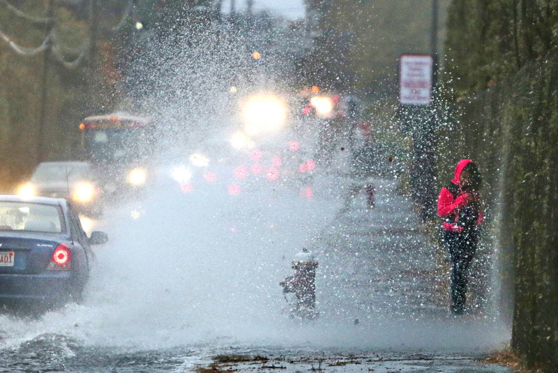 A student walking to school is doused by a wall of water being thrown up by a car driving over the high standing water on Parker Street in New Bedford. MA on a very wet morning. 