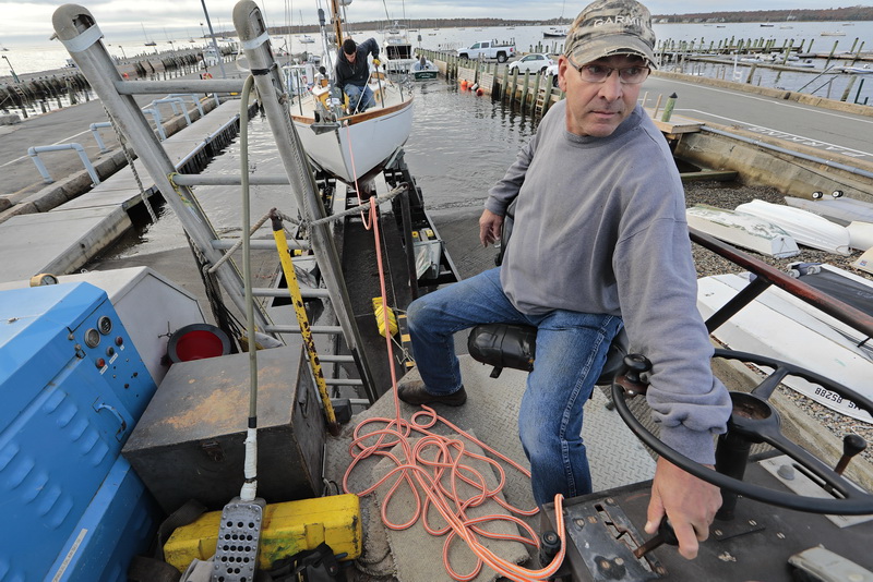 Bill Wilbur of Triad Boatworks drives the submersible unit boat carrier out of Mattapoisett, MA harbor as Silas Costa can be seen on deck preparing the rigging, as owners rush to remove their boats before an expected storm sweeps across the region.