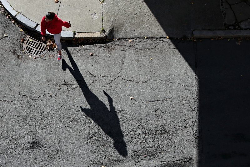 The morning sun casts a long shadow as a woman steps off of the curb to cross School Street in downtown New Bedford, MA.